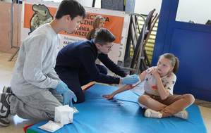 Dzieci udzielają pierwszej  pomocy medycznej rannej osobie. Opatrują rany