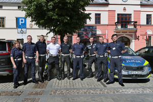 Policjanci Wydziału Ruchu Drogowego przed budynkiem Urzędu Miasta i Gminy w Olkuszu. Po prawej stronie oznakowany radiowóz