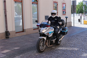 Policjant ruchu drogowego na motocyklu. W tle zabudowania i fragment olkuskiego Rynku