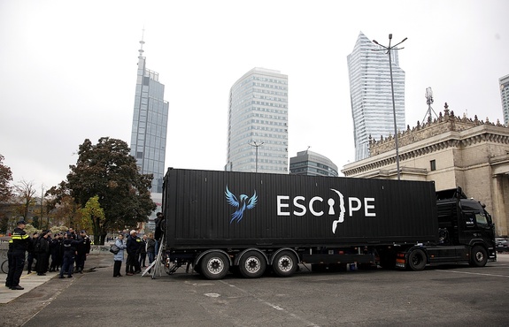Escape van przed którym gromadzą się ludzie. W tle miasto i zabudowania