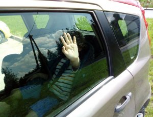 dziecko zamknięte w samochodzie. Trzyma rękę na szybie.