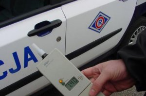 Urządzenie do badania stanu trzeźwości kierujących, alkomat trzymany w ręce w tle boczne drzwi radiowozu z napisem Policja.