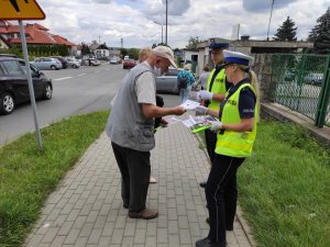 Policjantka ruchu drogowego wręcza starszemu mężczyźnie ulotki z informacja o oszustach.