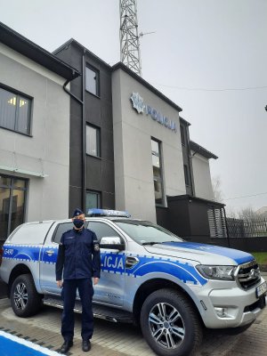 Nowoczesny radiowóz ford ranger. Obok umundurowany policjant. W tle nowy budynek Komisariatu Policji w Kluczach.