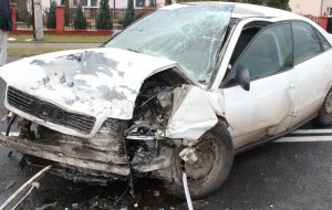 Audi po zderzeniu czołowym. Uszkodzony przód pojazdu, zniszczony zderzak, lampa, pokrywa silnika. Na szybie widać ślady uszkodzenia tzw. pajęczynka. Na drodze znajdują się elementy zderzaka i innych części samochodu .
