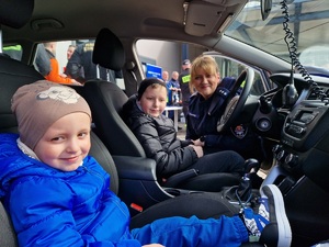 Policjantka przy radiowozie kuca przy dzieciach siedzących za kierownicą i po stronie pasażera