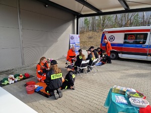 Przy trzech stanowiskach służby zdrowia siedzą dzieci z ochotniczych straż pożarnych w mundurach. Ratownicy pokazują jak udzielać pomocy medycznej na fantomach.