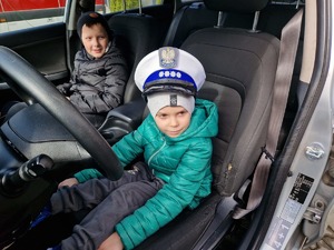Dzieci w radiowozie. Jedno z nich siedzące od strony kierowcy ma na głowie czapkę policjanta ruchu drogowego.