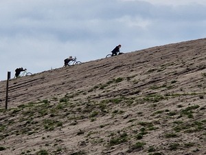 Rowerzyści pchają rowery pod górę usypaną piaskiem