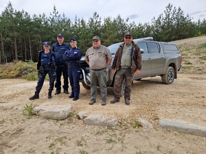 Policjanci i funkcjonariusze straży leśnej przy pojeździe służbowym straży. W tle pejzaż lasy i piaski