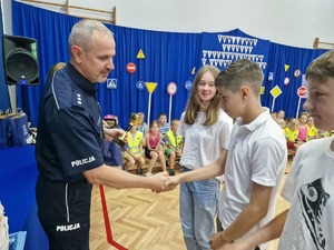 I Zastępca gratuluje laureatom konkursu i wręcza nagrody. W tle dzieci i młodzież