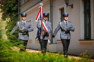 1.	Poczet sztandarowy w umundurowaniu galowym. Trzech policjantów krokiem defiladowym. W środku policjant trzyma sztandar Komendy Powiatowej Policji w Olkuszu.