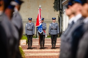 Poczet sztandarowy. Po obu stronach policjanci w rzędach.