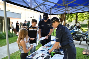 Policjantka i policjant przy stanowisku profilaktycznym policji podają dzieciom gadżety.