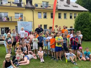 Dzielnicowy wraz pracownikami Sanepidu oraz dużą grupą dzieci wypoczywających na kolonii na terenie komisariatu w Kluczach. W tle budynek.