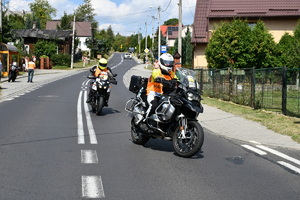 Motocykliści zabezpieczający wyścig kolarski. W tle ulica i zbudowania oraz gromadzący sie przy jezdni gapie.