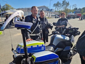 Policjant ruchu drogowego przy motocyklu obok dwaj motocykliści. Zdjęcie przy stanowisku profilaktycznym policji.