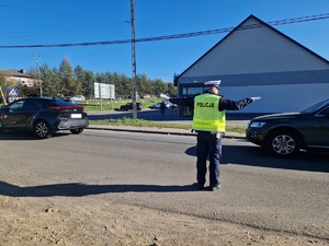 Policjant ruchu drogowego w odblaskowej kamizelce kieruje ruchem na drodze