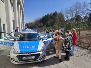 Uczniowie przy radiowozie przed budynkiem komendy