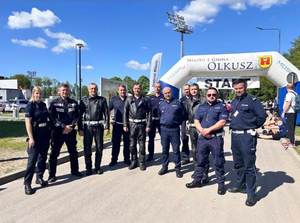 Policjanci ruchu drogowego wraz z Komendantem podczas zabezpieczenia rajdu rowerowego. W tle meta przejazdu