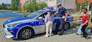 Dzieci w radiowozie. Obok kilu chłopców i policjant ruchu drogowego
