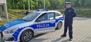 Dziecko za kierownica radiowozu obok policjant ruchu drogowego w białej czapce
