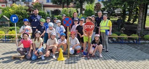 Policjanci z dziećmi podczas egzaminu. dzieci mają kaski na głowach, przy nich rowery i znaki drogowe