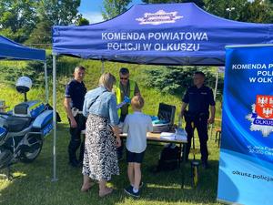 Policjanci pod namiotem pokazują sprzęt policyjny i rozmawiają z uczestnikami imprezy.