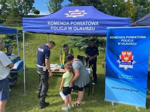 Policjanci pod namiotem pokazują sprzęt policyjny i rozmawiają z uczestnikami imprezy.