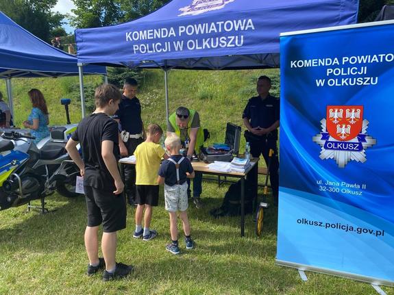 Policjanci pod namiotem pokazują sprzęt policyjny i rozmawiają z uczestnikami imprezy.