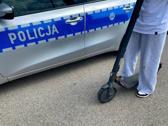 Zdjęcie osoby na hulajnodze na tle policyjnego radiowozu