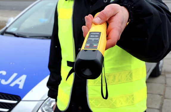 Policjant trzymający alkomat. W tle radiowóz policyjny.