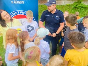 dzieci słuchające prelekcji. W tle pracownica sanepidu i policjant.