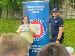 policjant i kobieta na tle baneru olkuskiego sanepidu.