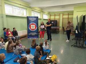 uczestnicy spotkania słuchający prelekcji. Na drugim planie policjant i pracownik sanepidu.