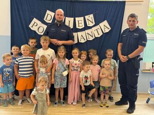 Dzieci pozujące do zdjęcia. Na drugim planie policjanci.