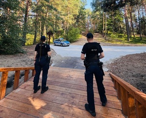 Policjanci na ścieżce. W tle radiowóz policyjny.