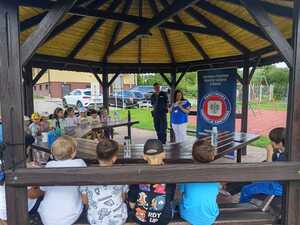 Dzieci słuchające przemówienia kobiety. Obok niej policjant.