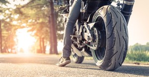 Fragment motocykla, na którym siedzi motocyklista.