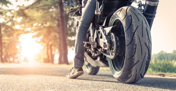 Fragment motocykla, na którym siedzi motocyklista.