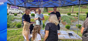 Uczestnicy wydarzenia i policjanci przy stoisku profilaktycznym. W tle fotograf.