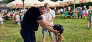 Policjant pokazujący dziecku policyjny sprzęt. W tle uczestnicy wydarzenia.