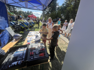Uczestnicy eventu przy stanowisku profilaktycznym w Olkuszu. W tle motocykle policyjne.