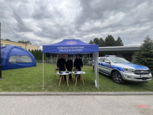 Policjanci na stanowisku profilaktycznym podczas Dni Wolbromia 2025. Obok radiowóz policyjny.