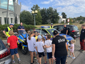 Grupa dzieci przy pojazdach policyjnych, w tle policjanci.