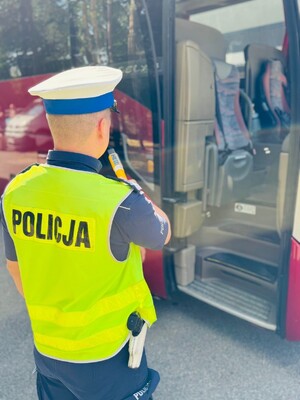 Policjant Ruchu Drogowego sprawdzający stan trzeźwości. W tle autokar.