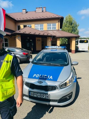 Policjant Ruchu Drogowego, obok radiowóz policyjny. W tle szkoła.