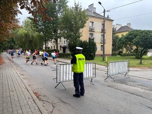 Policjant Ruchu Drogowego zabezpieczający bieg. Przed nim uczestnicy biegu.