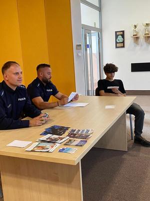 Policjancji z uczestnikiem gry przy biurku.