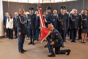 Pożegnanie mł. insp. Dominika Jurczaka ze sztandarem jednostki. W tle kadra kierownicza i goście.